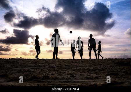 Gruppe von Menschen, die ein Fußballspiel am Strand bei Sonnenuntergang genießen, Silhouetten vor einem Hintergrund der Wolken, La Digue, Seychellen, Afrika Stockfoto