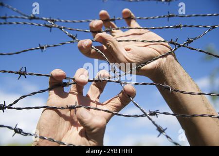 Hände greifen der Stacheldraht im Zeichen weg mit dem blauen Himmel Hintergrund ausgeführt Stockfoto