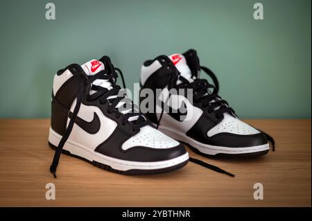 Schwarz-weiße Nike Dunk High Sneakers auf Holzregal mit hohem Design und rotem Nike Logo an der grünen Wand Stockfoto