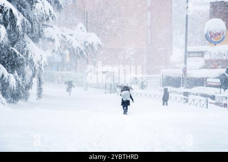 Madrid, Spanien, 9. Januar 2021: Menschen gehen auf einer schneebedeckten Straße der Stadt bei starkem Schneefall mit umgestürzten Bäumen. Sturm Filomena in Madrid. Kunst Stockfoto
