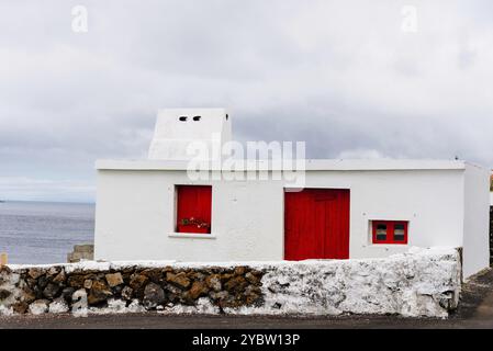 Gemütliches Fischerhaus in Weiß mit roten Fenstern und Türen im Dorf Porto Judeu auf der Insel Terceira, Azoren-Archipel Stockfoto