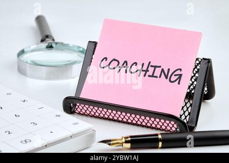 Geschäftskonzept. Der Satz, Text, Wortwahl COACHING ist auf einem pinkfarbenen Aufkleber auf einem schwarzen Ständer auf grauem Hintergrund geschrieben. Stockfoto