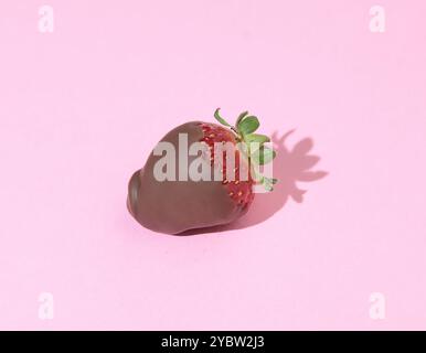 Ganze isolierte Erdbeere mit Schokoladenüberzug auf rosa Hintergrund mit Schatten für Design. Essen und Nachtisch. Stockfoto