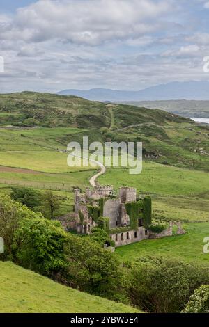 Vertikales Foto der Ruinen von Clifden Castle in Connemara, Irland, inmitten von sanften grünen Hügeln und gewundenen Pfaden. Die mit Efeu bedeckte Struktur zeichnet sich durch einen aus Stockfoto