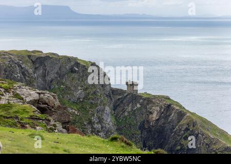 Blick auf zerklüftete Klippen, die Meer und Himmel in der Nähe von Slieve League, Irland, treffen, mit einem alten Steinbau am Rand Stockfoto