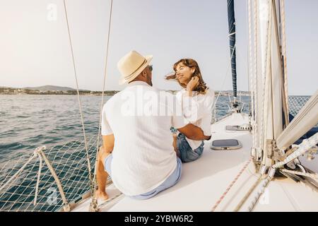 Ein fröhliches Paar genießt einen sonnigen Tag auf einem Segelboot, umgeben von einer ruhigen Aussicht auf das Meer. Die Szene fängt Romantik, Entspannung und Abenteuer auf einem bea ein Stockfoto