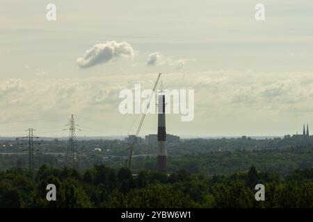 Arbeiten Sie oben auf dem Kamin. Ein hängender Bagger an einem Kran zerstört einen Schornstein. Drohnenansicht des Abbruchs des Schornsteins, Bagger arbeitet mit Rauch Stockfoto