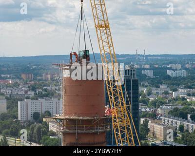 Arbeiten Sie oben auf dem Kamin. Ein hängender Bagger an einem Kran zerstört einen Schornstein. Drohnenansicht des Abbruchs des Schornsteins, Bagger arbeitet mit Rauch Stockfoto