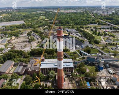 Arbeiten Sie oben auf dem Kamin. Ein hängender Bagger an einem Kran zerstört einen Schornstein. Drohnenansicht des Abbruchs des Schornsteins, Bagger arbeitet mit Rauch Stockfoto