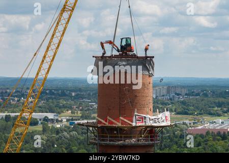 Arbeiten Sie oben auf dem Kamin. Ein hängender Bagger an einem Kran zerstört einen Schornstein. Drohnenansicht des Abbruchs des Schornsteins, Bagger arbeitet mit Rauch Stockfoto