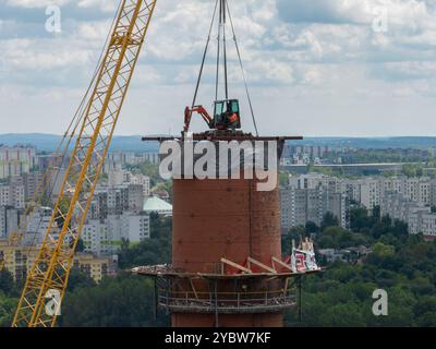 Arbeiten Sie oben auf dem Kamin. Ein hängender Bagger an einem Kran zerstört einen Schornstein. Drohnenansicht des Abbruchs des Schornsteins, Bagger arbeitet mit Rauch Stockfoto