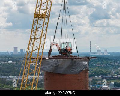 Arbeiten Sie oben auf dem Kamin. Ein hängender Bagger an einem Kran zerstört einen Schornstein. Drohnenansicht des Abbruchs des Schornsteins, Bagger arbeitet mit Rauch Stockfoto