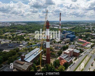 Arbeiten Sie oben auf dem Kamin. Ein hängender Bagger an einem Kran zerstört einen Schornstein. Drohnenansicht des Abbruchs des Schornsteins, Bagger arbeitet mit Rauch Stockfoto