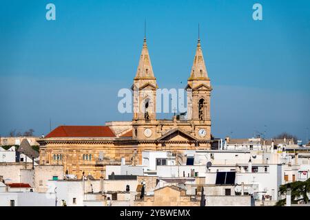 Blick auf die Basilica dei SS. Medici Cosma e Damiano in Alberobello, Italien, mit seinen berühmten Doppeltürmen, die sich über den weißen Dächern der Stadt erheben. Stockfoto