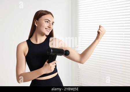 Frau, die das Schlaggerät benutzt, um den Bizeps drinnen zu entspannen Stockfoto