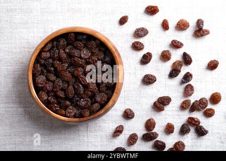 Gewöhnliche kommerzielle Rosinen, in einer Holzschale auf Leinenstoff. Dunkle getrocknete große, kernlose Traubenrosinen, roh gegessen oder zum Kochen verwendet. Stockfoto