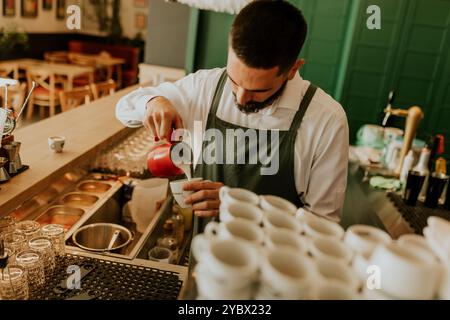 In einem warmen und einladenden Café gießt ein engagierter Barista fachmännisch Milch in eine Kaffeetasse und sorgt so für ein angenehmes Erlebnis für Gäste. Stockfoto