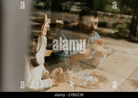 In einer warmen und einladenden Atmosphäre lacht ein Paar, während es Pizzascheiben genießt, umgeben von Grün und guter Atmosphäre. Stockfoto
