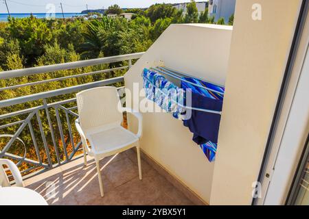 Trocknende Kleidung auf Balkonregal mit Plastikstuhl und Blick auf grüne Bäume und das Mittelmeer im Hintergrund. Kreta. Griechenland. Stockfoto