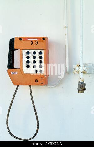 Dieses Bild zeigt ein nostalgisches maritimes Telefon, das an der weißen Wand eines Schiffes befestigt ist und alte Kommunikationswerkzeuge mit der Einfachheit eines Minimalis verbindet Stockfoto