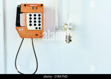 Dieses Bild zeigt ein Vintage-Telefon, das an der weißen Wand eines Schiffes befestigt ist und das Wesen traditioneller maritimer Kommunikationsgeräte in einem Minim erfasst Stockfoto