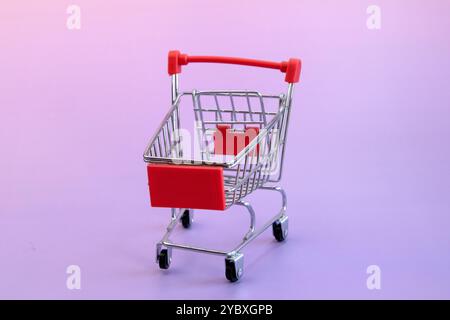 Kleiner Miniatur-Supermarkt-Trolley auf hellviolettem Hintergrund, Nahaufnahme mit leerem Raum Vorderansicht Stockfoto