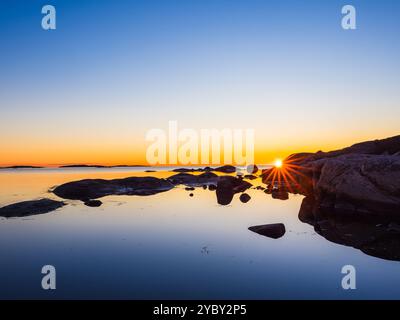 Ein atemberaubender Sonnenuntergang wirft ein warmes Leuchten über die schwedische Küste und erhellt das ruhige Wasser. Silhouettenfelsen schaffen eine ruhige Atmosphäre wie Day tran Stockfoto