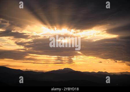 Landschaft eines Sonnenuntergangs über den Bergen, in der die Sonne mit großen Strahlen zu sehen ist, die durch die Wolken gehen, bevor sie sich hinter den Bergen verstecken Stockfoto