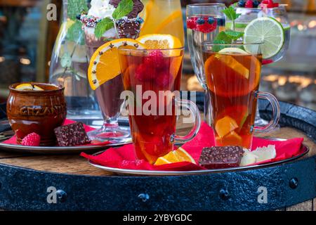 Eine Auswahl an warmen Getränken: Glühwein, heißer Tee mit Gewürzen und heiße Schokolade serviert mit Stücken Orange, Limette, Zitrone und Beeren Stockfoto