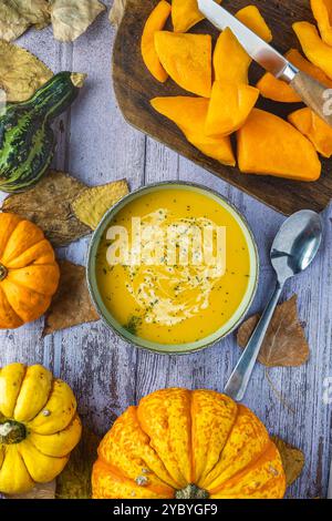 Stillleben von Kürbissen auf Herbstblättern, Schneidebrett, Messer und gehacktem Kürbis, im mittleren Teil eine Schüssel mit Kürbissuppe, Blick von oben. Stockfoto