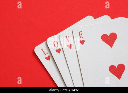 Liebe finden. Vier Spielkarten zaubern Liebe auf rotem Hintergrund und wecken Leidenschaft und Glück. Perfekt für Jubiläen, Hochzeiten oder valentinstag. Cele Stockfoto