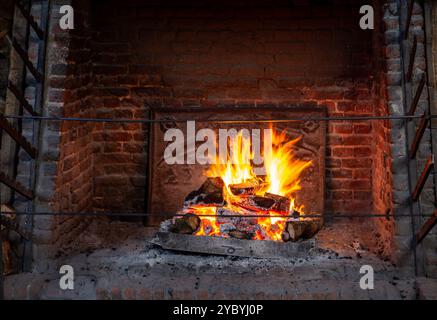 Ein großer offener Tudor-Küche-Kamin im Hampton Court Palace mit hell brennenden Baumstämmen und Spießstäben Stockfoto