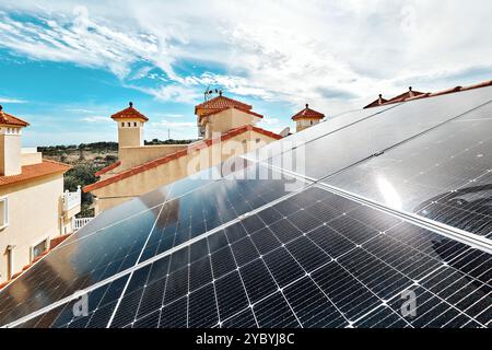 Solarpaneele auf rot gekachelten Dächern des Wohngebäudes auf sonnigem bewölktem Himmel Hintergrund installiert. Erneuerbare Energiequellen, umweltfreundliche Wohnräume Stockfoto