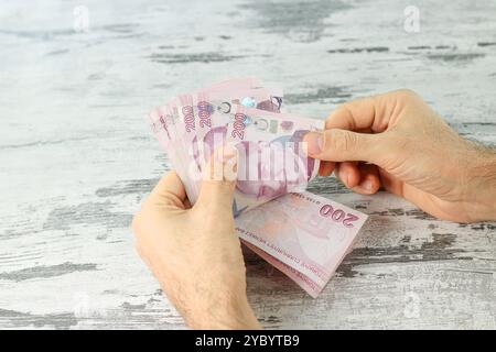 Die Hand des Mannes zählt 200-Lira-Türkische Banknoten auf weißem Holztisch. Nahaufnahme. Stockfoto