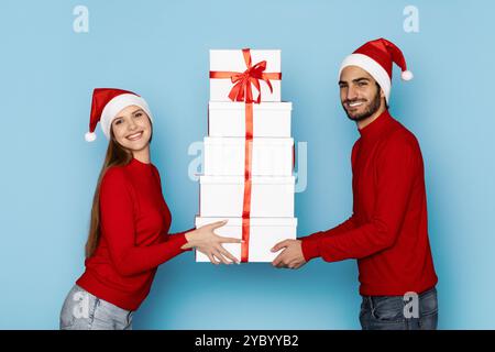 Glückliches Paar in festlichen Hüten, die Geschenke auf blauem Hintergrund austauschen Stockfoto