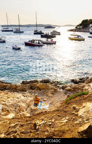 Frauen entspannen an einem felsigen Strand an einem sonnigen Tag am Hvar Park Uferpromenade, Insel Hvar, Kroatien Stockfoto