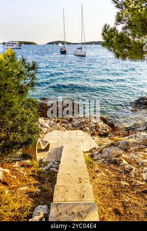 Kleiner felsiger Strand und Segelboote vor Anker am Meer entlang der Küste des Hvar Park, Insel Hvar, Kroatien Stockfoto