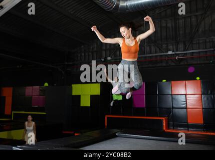 Glückliche Frau mittleren Alters, die auf Trampolinen in einem Sporthalle trampoliniert und springt, Workout und modernes Unterhaltungskonzept Stockfoto
