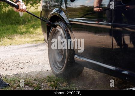 Eine Nahaufnahme eines schwarzen Fahrzeugrads, das mit einem Hochdruckreiniger gereinigt wird. Stockfoto