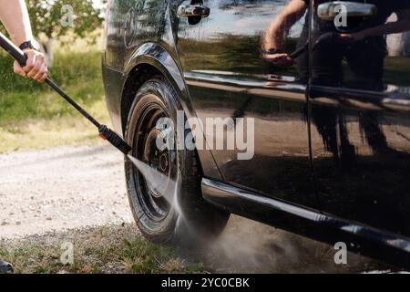 Dynamische Autowaschanlage mit Handschuhen und Druckwaschanlage an einem schwarzen Fahrzeugrad. Stockfoto