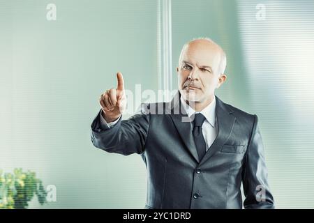 Ein Mann in Anzug mittleren Alters weist selbstbewusst und schlägt einen wichtigen Geschäftsvorschlag oder eine entschlossene Maßnahme in einem Unternehmensumfeld vor Stockfoto