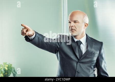 Ernsthaft aussehender männlicher, kahlköpfiger und in formeller Kleidung zeigt direkt und betont einen wichtigen Punkt in einem geschäftlichen Meeting Stockfoto