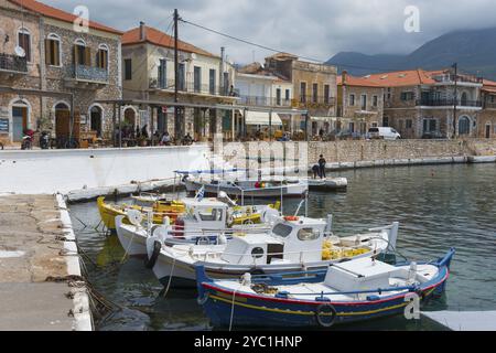 Kleiner Hafen mit Fischerbooten vor einer Reihe von traditionellen Steinhäusern an der Küste mit Bergkulisse, Agios Nikolaos, Mani, Messenia Stockfoto