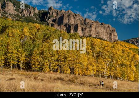 Ein Paar und ihr Hund genießen die Landschaft der vulkanischen Tuffklippen von High Mesa im oberen Cimarron Valley von Colorado mit Espenbäumen im vollen Herbst Stockfoto