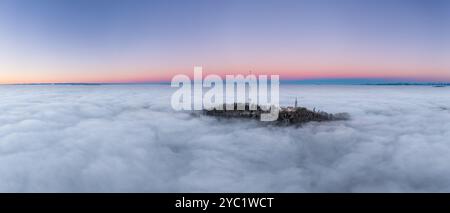 Atemberaubender Blick aus der Luft auf einen Berggipfel über den Wolken bei Sonnenaufgang mit pastellfarbenem Himmel, Uetliberg Zürich Stockfoto