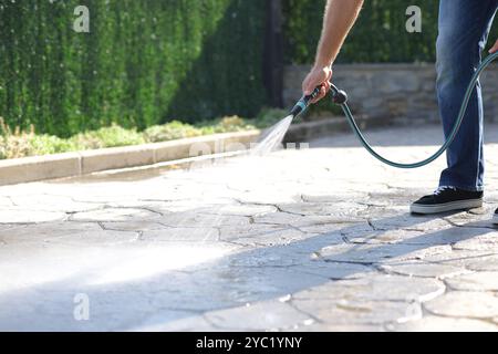 Nahaufnahme eines Mannes, der den Gartenboden mit Wasser mit einem Schlauchschlauch reinigt Stockfoto