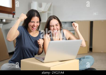 Aufregende Mitbewohner, die einen Laptop überprüfen, um gute Nachrichten zu feiern und das Haus zu renovieren Stockfoto