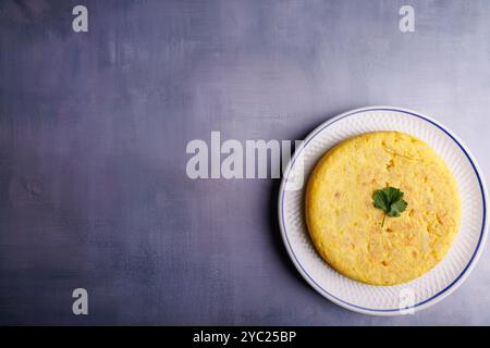 Ein köstliches spanisches Kartoffelomelett sitzt in einer Ecke des Rahmens und zeigt seine goldene Textur auf der blauen Tischplatte aus Beton Stockfoto