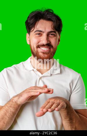Ein junger Mann in einem weißen Poloshirt tanzt energisch vor einem leuchtend grünen Hintergrund Stockfoto
