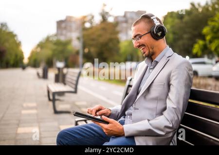 Porträt eines glücklichen Geschäftsmannes, der Nachrichten auf einem digitalen Tablet sendet. Mann, der in der Stadt auf einer Bank sitzt und ein digitales Tablet benutzt. Stockfoto